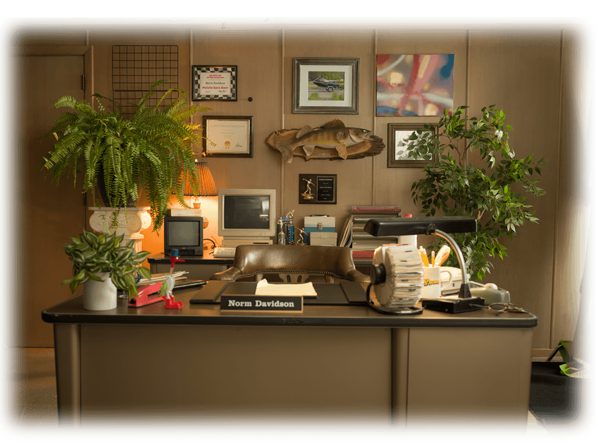 Image of Norm’s office, cluttered with retro items and silly tchochkes, including an old computer, a tube TV, a rolodex, and a singing fish.